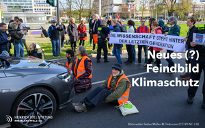 Das Bild zeigt Aktivist*innen der letzten Generation, die ein Auto blockieren und von der Polizei umstellt sind mit der Aufschrift: "Neues (?) Feindbild Klimaschutz?"
